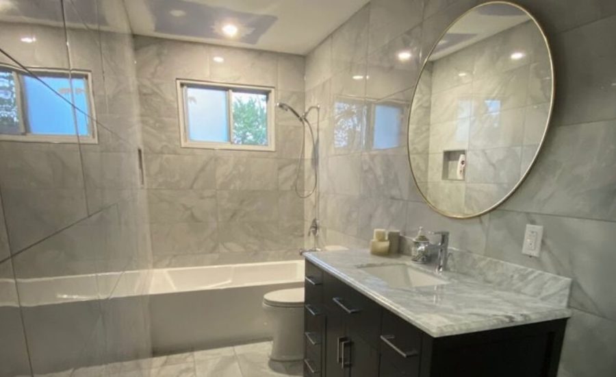 Remodeled bathroom with marble-look porcelain tile, a tiled tub-shower and a round mirror over a dark vanity