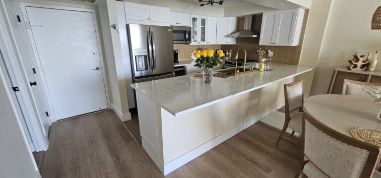 Entry of a remodeled condo unit opening onto a white shaker kitchen with a quartz island