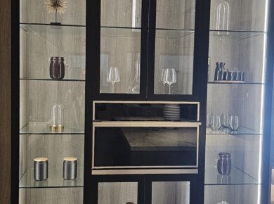 Showroom display of tall black-framed glass-front cabinets with lit glass shelves